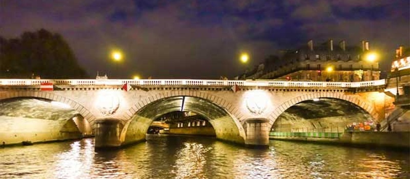 Pont illuminé et reflets sur la Seine à la nuit tombée