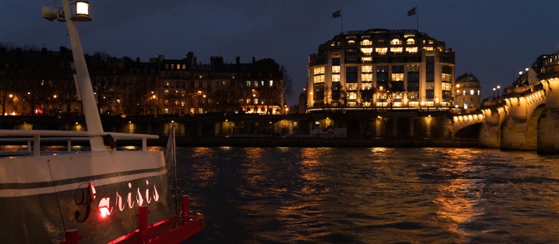 Bateau Parisis sur la Seine, devant les bâtiments et un pont illuminés de Paris
