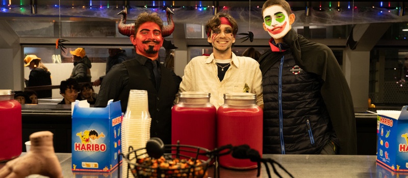 Trois hommes déguisés pour Halloween derrière le bar, avec des bonbons et une araignée décorative