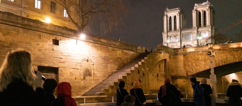 Passagers sur le bateau au pied des quais, avec les tours illuminées de Notre-Dame de Paris